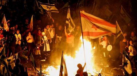 Protesters waving flags around fires in Tel Aviv