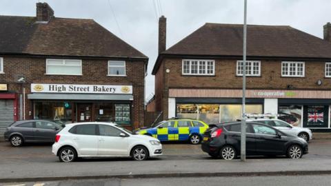 Parade of shops including bakery and Co-op with police car parked outside