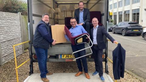 Four men standing at the back of a lorry with donations