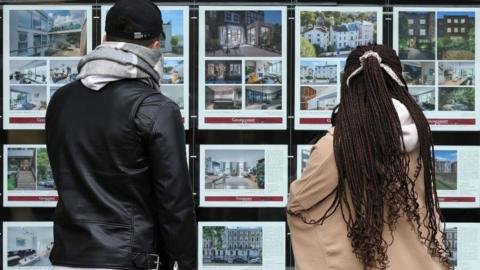 People looking at property adverts in an estate agent's window