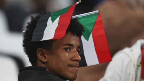 A young Sudan fan wears two Sudan flags on his head