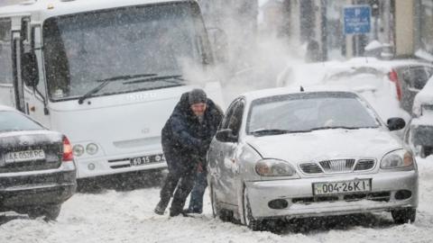 A man pushes a car trapped in snow at a street as snow falls in central Kiev,