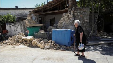 Woman walks near damaged building in Arkalochori, Crete