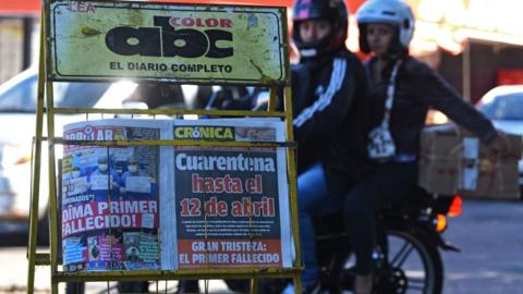 A motorcycle rides near a stall displaying front pages of newspapers with the news of the first person killed by the new coronavirus, in Asuncion on March 21, 2020.