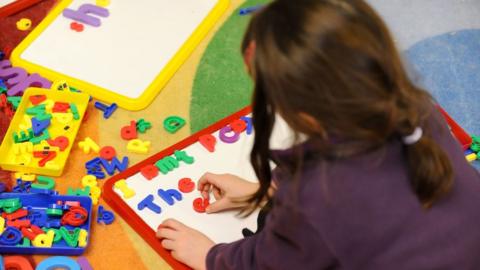 A child playing with colourful magnetic letters on a white board.