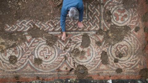 a mosaic being uncovered by a man in a blue shirt