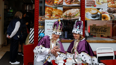 Royal fans dressed in royal-themed costumes sit outside a bar while waiting for the Coronation concert at Windsor Castle