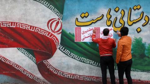 Two men put campaign posters on a wall in Tehran