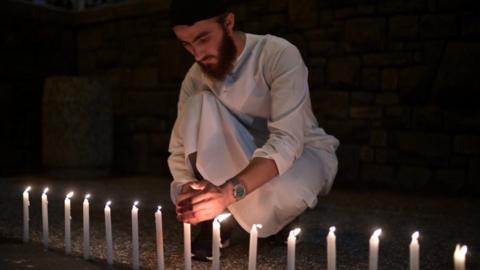 A well-wisher helps to light 49 candles as he pays respects to victims outside the hospital in Christchurch on March 16, 2019