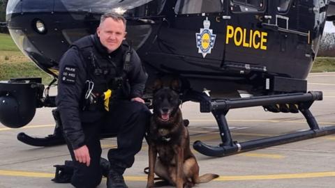 PC Dan Kemble with PD Ronnie with a helicopter behind them
