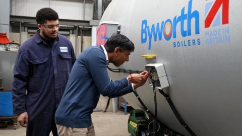 Britain's Prime Minister Rishi Sunak helps to wire up a boiler with an apprentice, during his visit to Byworth Boilers at the Parkwood Boiler works in Keighley, Britain