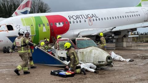 Firefighters next to small aircraft with larger plane in background