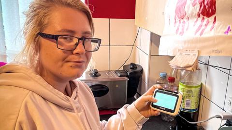 Nikita Harris holding a smart meter in her kitchen
