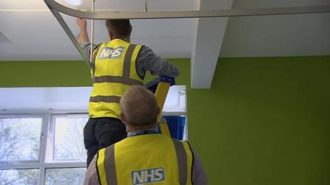 Workmen inspecting the roof of a hospital affected by the RAAC plank problem