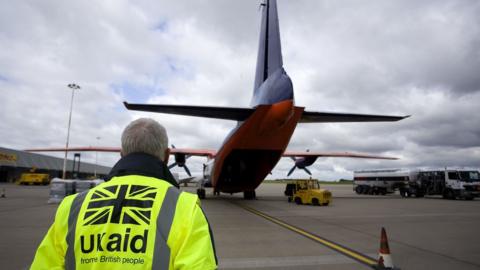 A UK aid staff member watches as cargo is loaded onto a plane