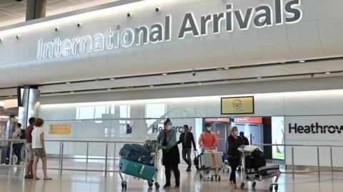 People pass through international arrivals wearing masks