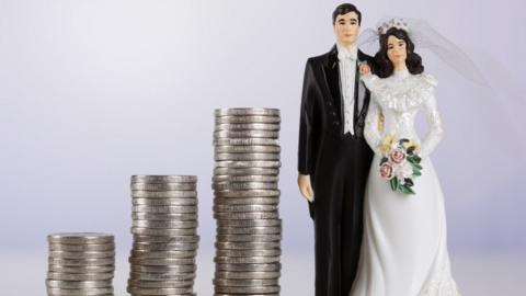 Miniature bride and groom models standing next to a stack of coins