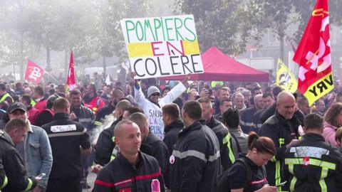 Firefighters stand with flags and banners to protest in Paris