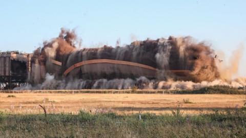 The building in mid collapse with plumes of smoke and dust rising