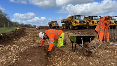 A man digs in the ground with machinery behind him