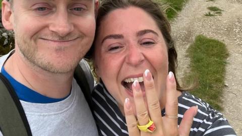 Becky Herbert holding up her hand with an engagement ring, standing next to her fiance Jules