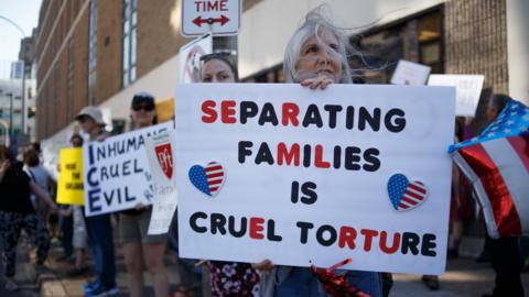 A woman holds a sign saying "separating families is cruel torture"