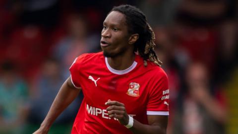 Tariq Uwakwe running with the ball on the pitch during a game for Swindon