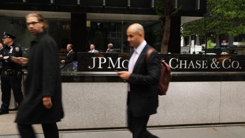 People walk past as others protest outside of the New York City headquarters of JPMorgan Chase on May 11, 2017 in New York City