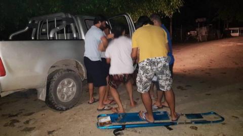 Men at the camp lifting a collapsed refugee into a PNG immigration car