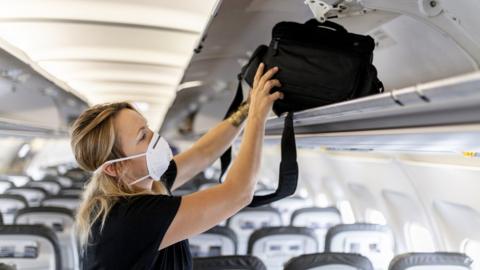 Woman puts bag into overhead locker in airplane