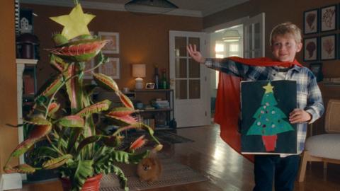 Young boy standing next to festive Venus flytrap in the John Lewis 2023 Christmas advert
