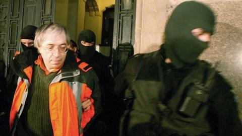 Bivolaru in orange jacket and masked police officer