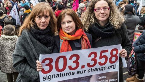 Activists pose in front of the protesting crowd, holding the number of signatures on the petition.