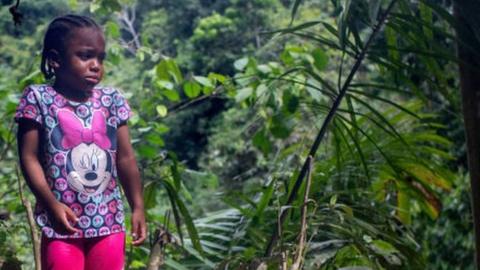 A Haitian girl waits for her mother to catch up after a guide had carried her up a mountain slope near Colombia's border with Panama on October 20, 2021