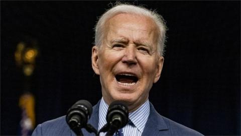 Joe Biden speaking at a microphone with his mouth open