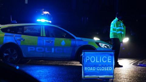 A police officer and police car with a road closure sign at night