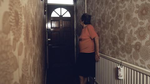 Vulnerable person standing behind front door