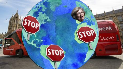 A globe with "stop" signs across various countries and Theresa May's face covering the UK.