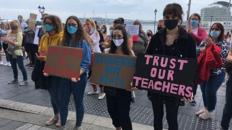 Myfyrwyr yn dal baneri mewn protest yn erbyn eu graddau Safon Uwch