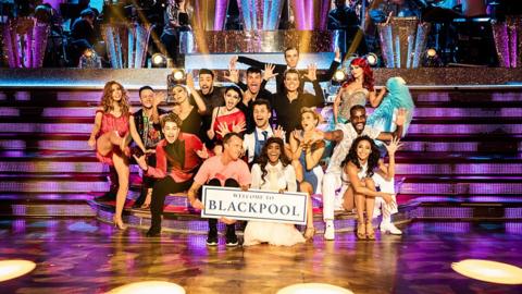Strictly dancers pose at the ballroom holding a Blackpool sign