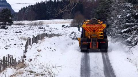 A snow plough spreads grit onto the road following heavy overnight snowfall