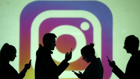 Silhouettes of mobile users are seen next to a screen projection of Instagram logo in this picture illustration taken March 28, 2018.