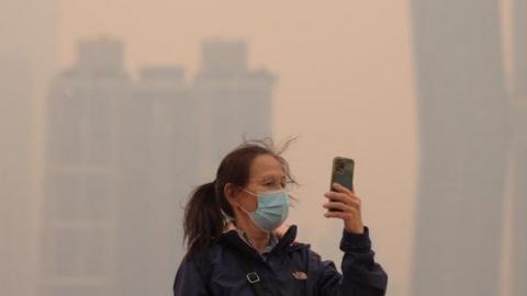 A person wearing a mask uses a cell phone in the hazy conditions