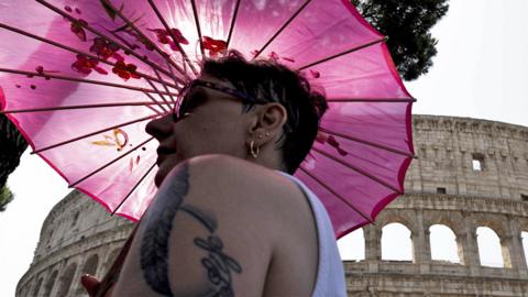 A woman holds an umbrella for sun protection near the Colosseum during a heat wave in Rome, Italy, on 18 July 2023