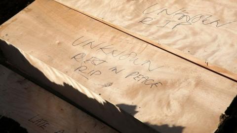 A wooden casket has words written on it "Unknown rest in peace, RIP"