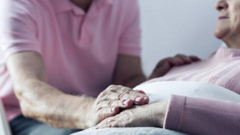 Older couple - with one placing hand on woman's who is lying down