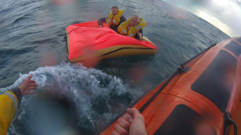 The pilots in their life raft with a hand out from the RNLI crew