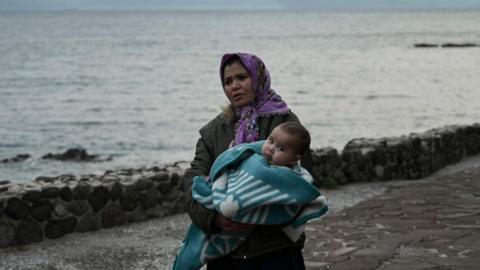 A migrant woman carries a toddler on Lesbos