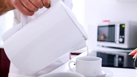 Someone pouring hot water out of a kettle into a cup