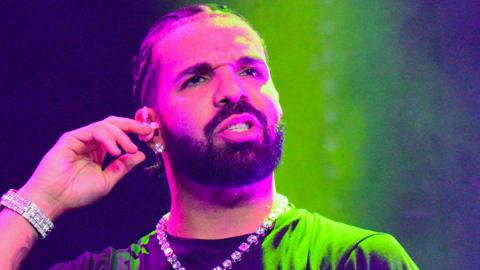 The rapper Drake, cast in green light, looking confused and with a finger in his right ear